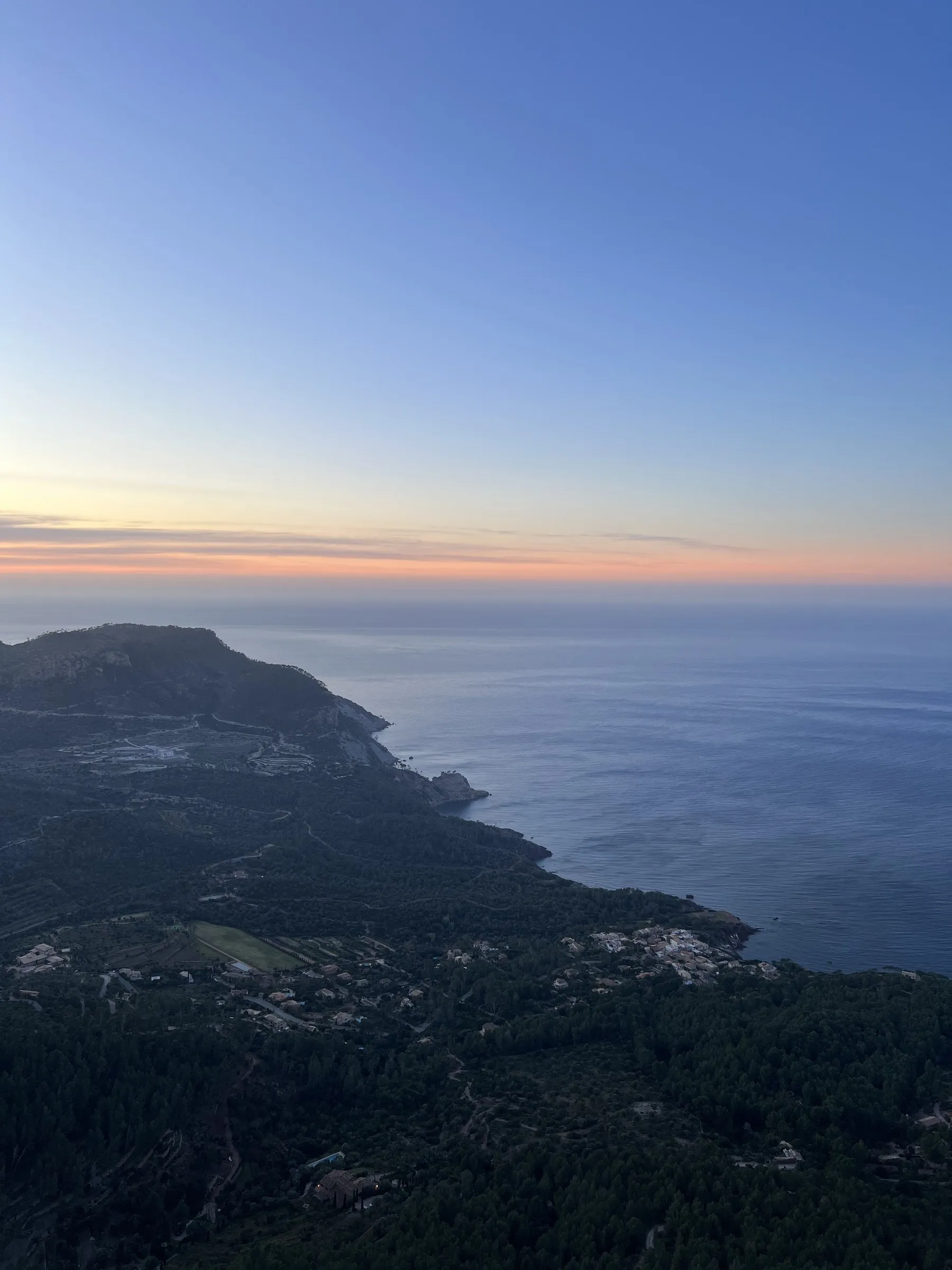 The coast at Banyalbufar at sunset, terraces dropping towards the sea and a headland against the water.