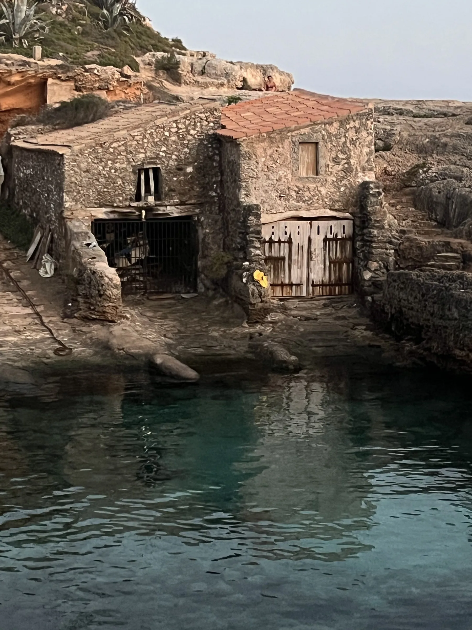 Ein steinernes Bootshaus mit Holztor und Ziegeldach, direkt über dem Wasser in den Fels gebaut.