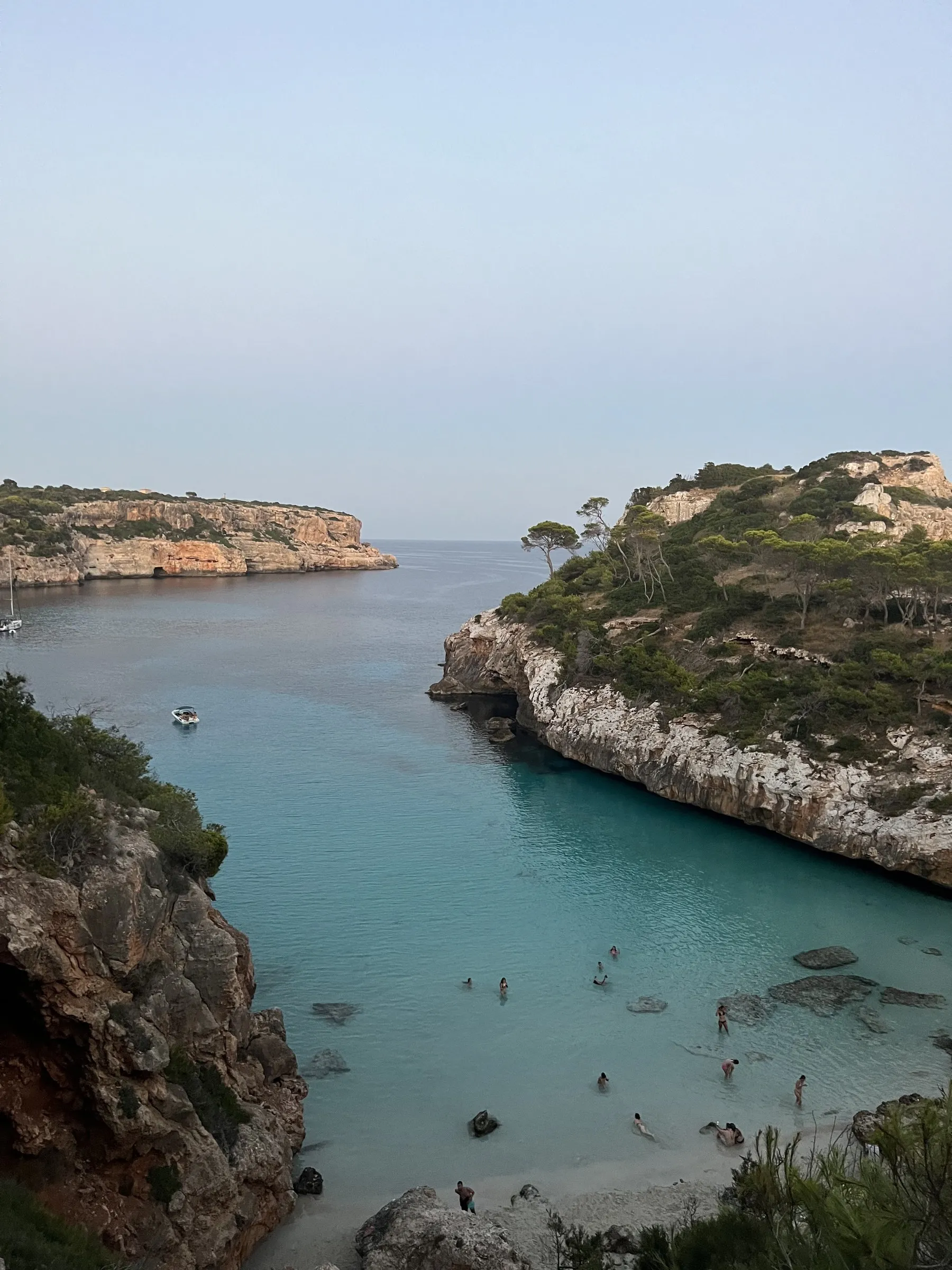 The narrow strip of sand at Caló des Moro wedged between cliffs, with swimmers in turquoise water and a boat at anchor.