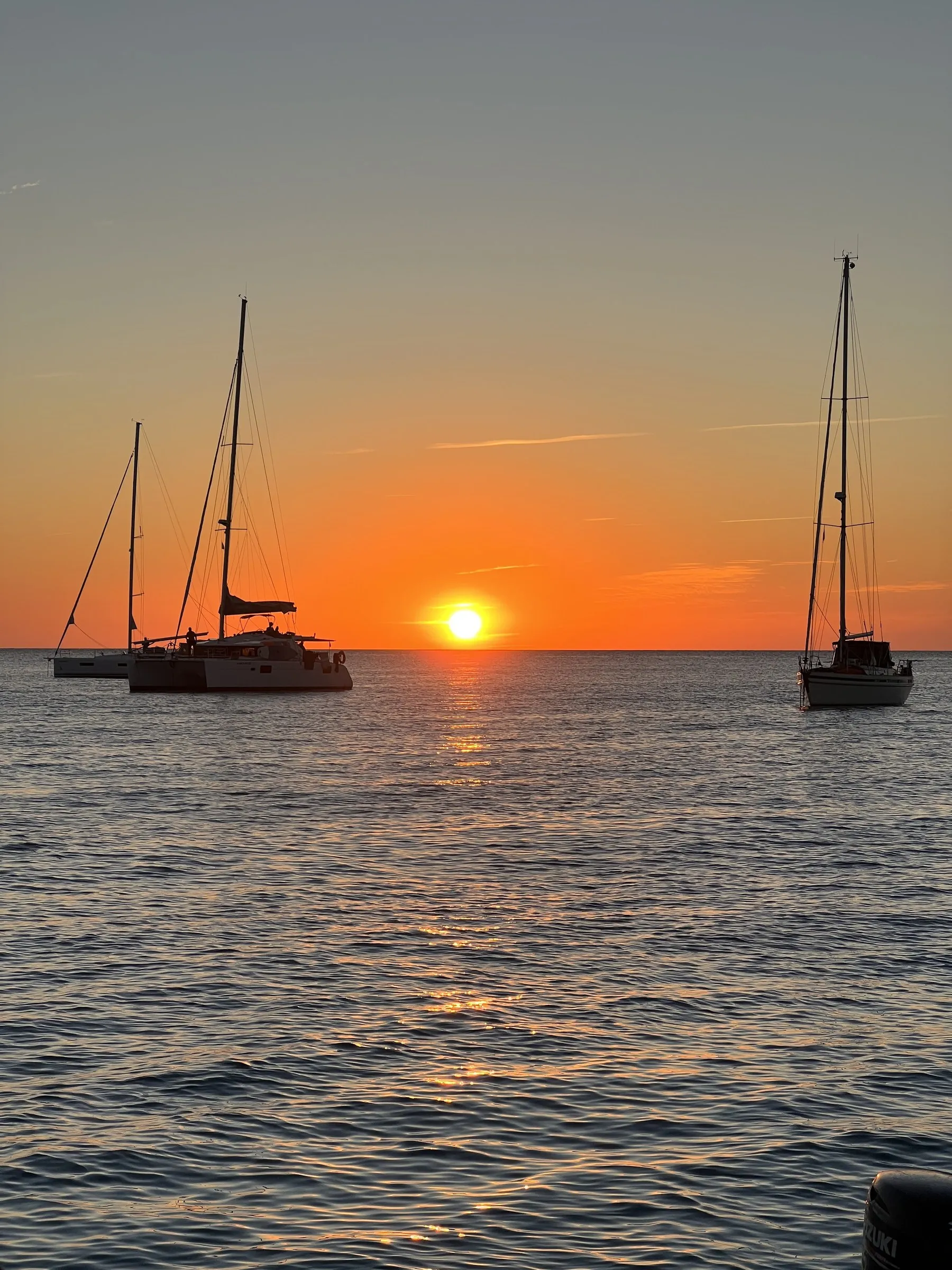 Two anchored sailing boats silhouetted against the setting sun off Cap de ses Salines.