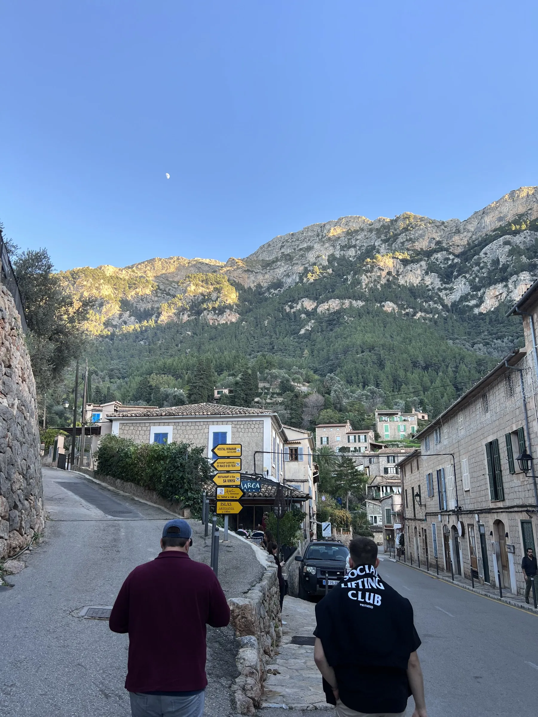 The main street of Deià on a winter afternoon, stone houses and the mountains lit by the last sun.