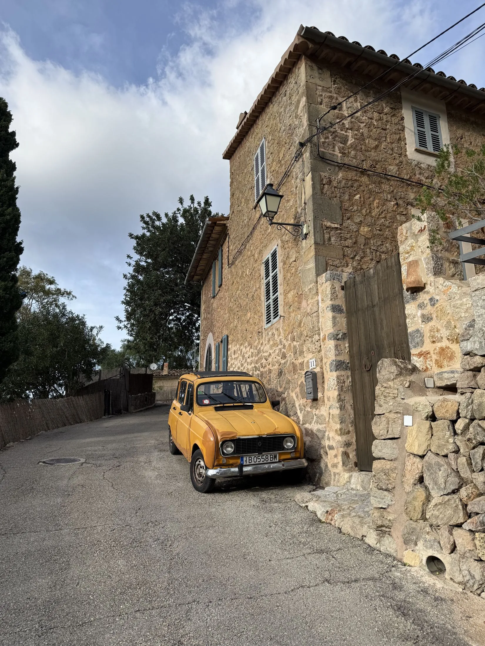 Una casa de piedra en una calle en cuesta de Deià, con un coche clásico amarillo aparcado delante